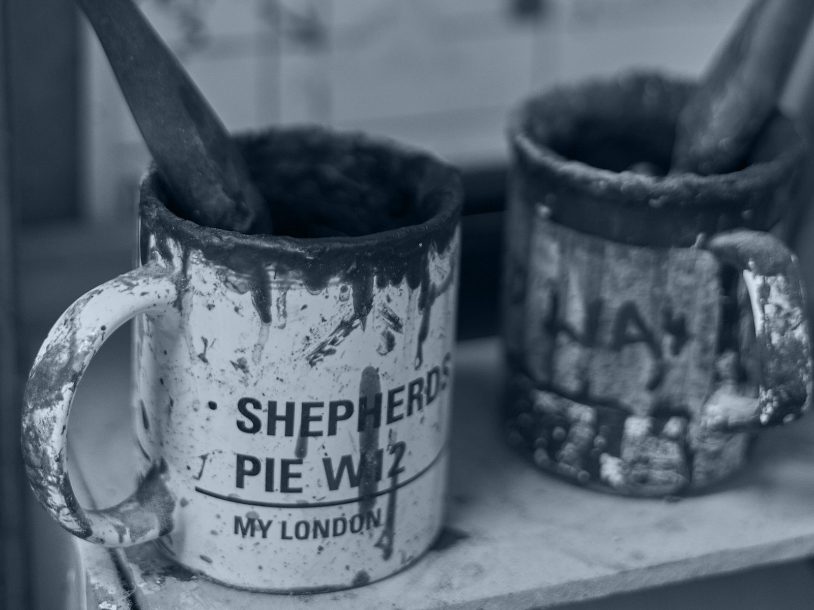 Gilding and finishing brushes standing in paint-marked enamel mugs on the Speedframe workshop bench